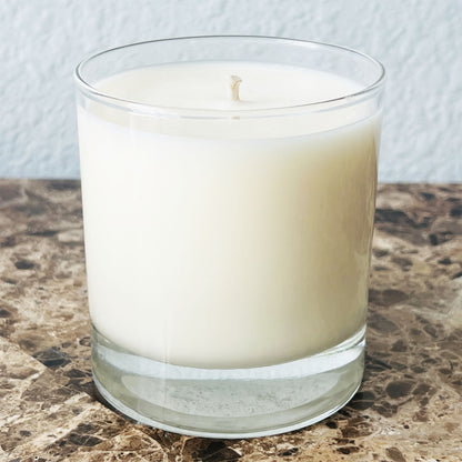 11oz candle in a clear glass container on a marble surface with a light blue textured background