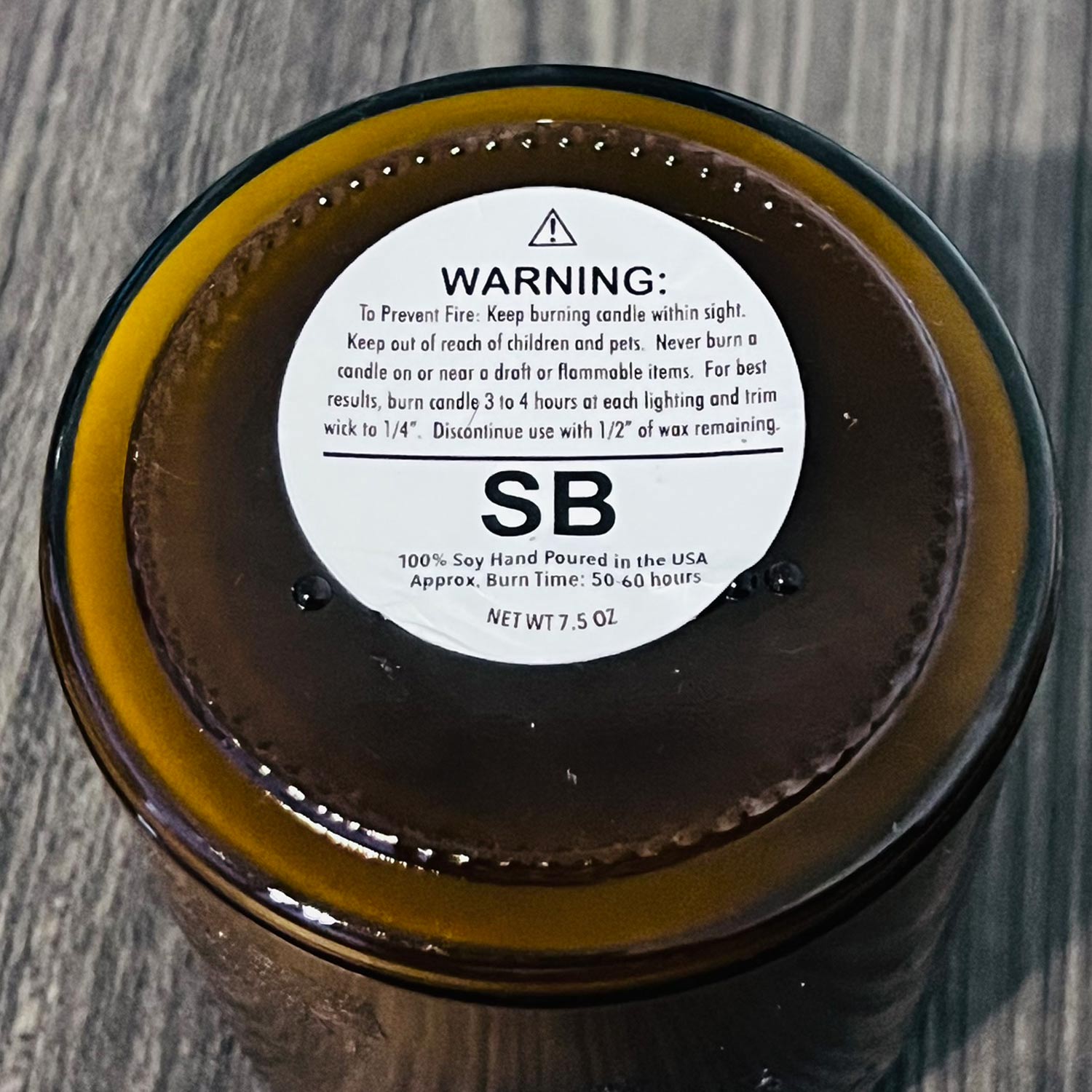 Candle jar lid with warning label and brand name on a wooden surface