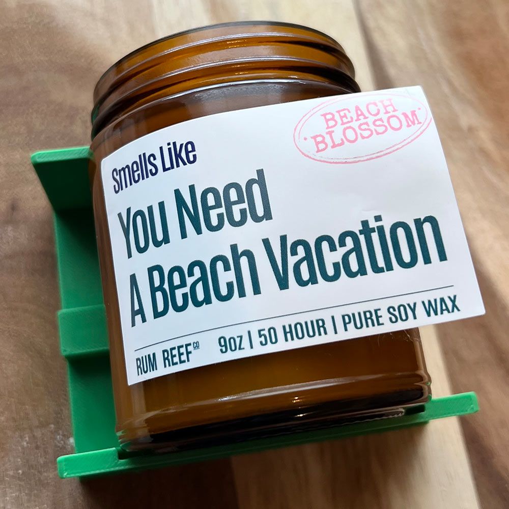 Jar of candle labeled 'You Need a Beach Vacation' with 'Beach Blossom' branding on a wooden surface.