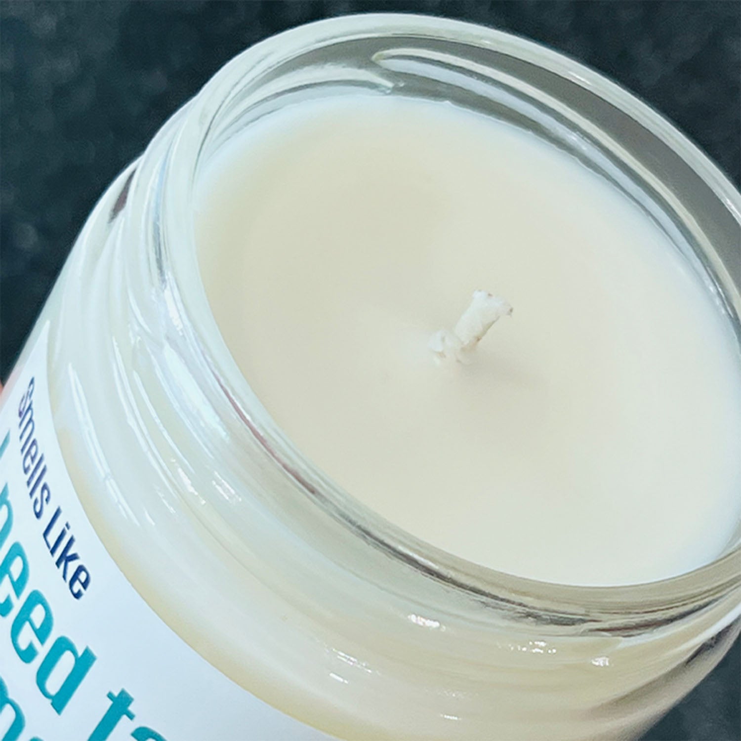 Close-up of a candle in a glass jar with a white wick against a dark background
