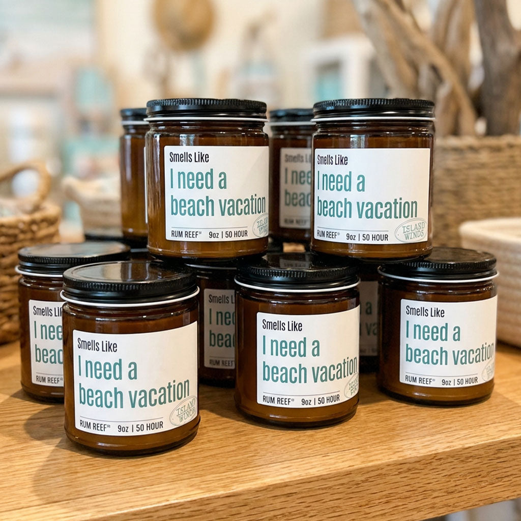 A group of amber glass candles with black lids and white labels reading 'Smells Like I need a beach vacation' arranged on a wooden surface with a softly blurred indoor background.
